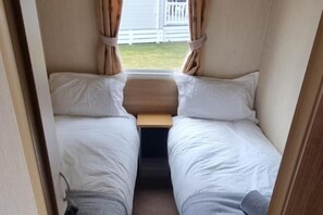 Interior de una caravana compacta, con dos camas, una mesita y cortinas.