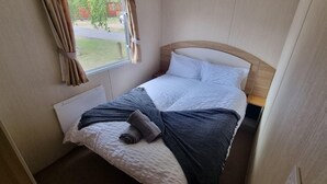 A small, neatly made bed with a white headboard, a grey blanket, and a rolled-up towel. - Petfriendly- Familyfriendly- 8berth- Tattershall (Lincoln)