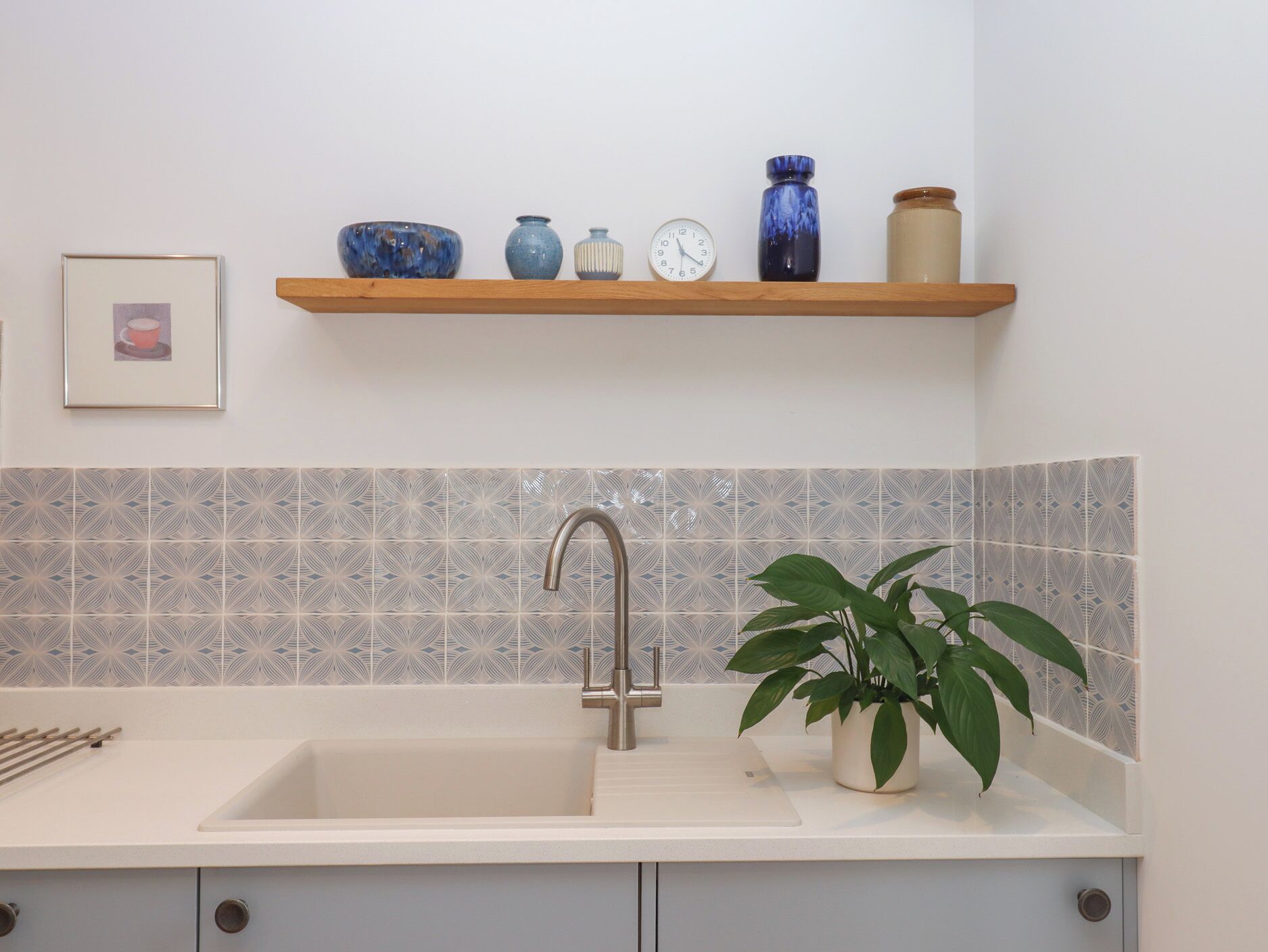 A kitchen with a sink, a plant, and a shelf with decorative items.