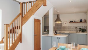Une cuisine moderne avec un escalier en bois, un coin repas avec de la vaisselle bleue et un îlot de cuisine agrémenté d’une bouteille et de verres.