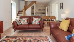 Un salon spacieux avec un canapé en cuir marron, un tapis à motifs et un escalier en bois menant à la cuisine.