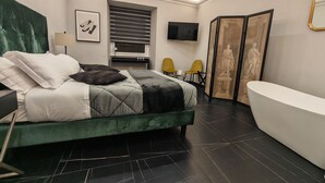 A modern bedroom with a large bed, a flat-screen TV, a bathtub, and a seating area with chairs. - AD Vatican Luxury Rooms (Rome)