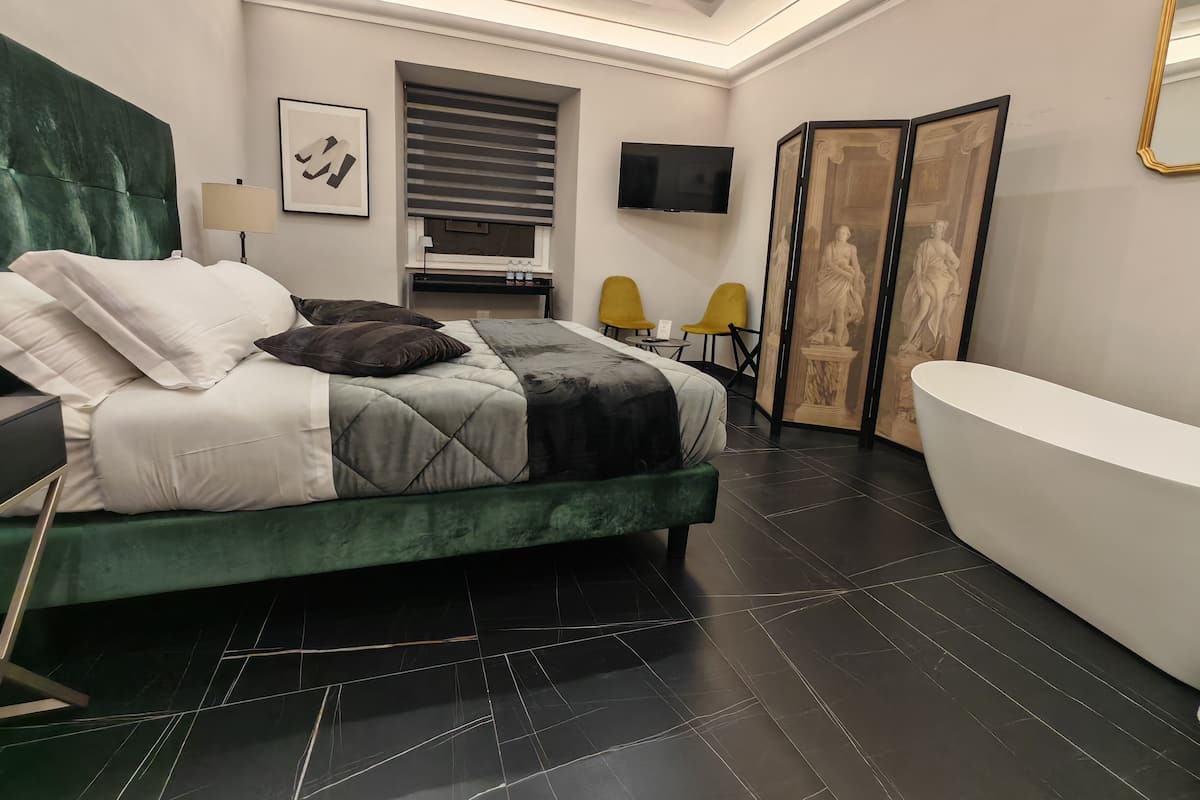 A modern bedroom with a large bed, a flat-screen TV, a bathtub, and a seating area with chairs.
