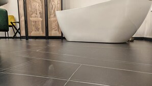 A modern bathroom with a freestanding bathtub, dark tiled flooring, and a decorative panel with classical sculptures. - AD Vatican Luxury Rooms (Rome)