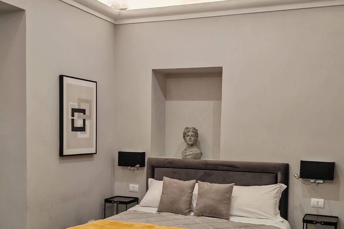 A modern bedroom with a large bed, a bust sculpture, and a framed picture on the wall.