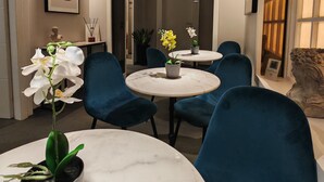 A modern dining area with round marble tables, blue upholstered chairs, and pendant lighting. - AD Vatican Luxury Rooms (Rome)