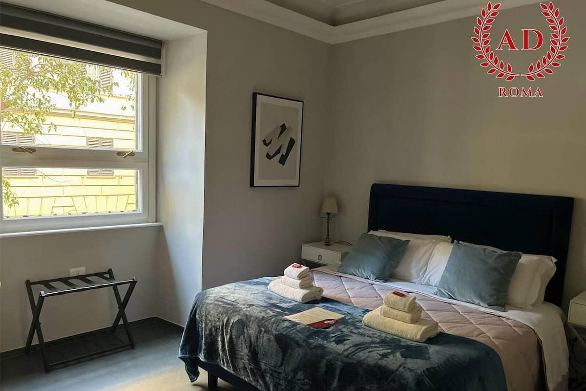 A bedroom with a bed, a nightstand, a window, and a towel rack.