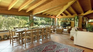 Een ruime eethoek met houten tafels en stoelen, een groot vloerkleed en uitzicht op groen buiten.