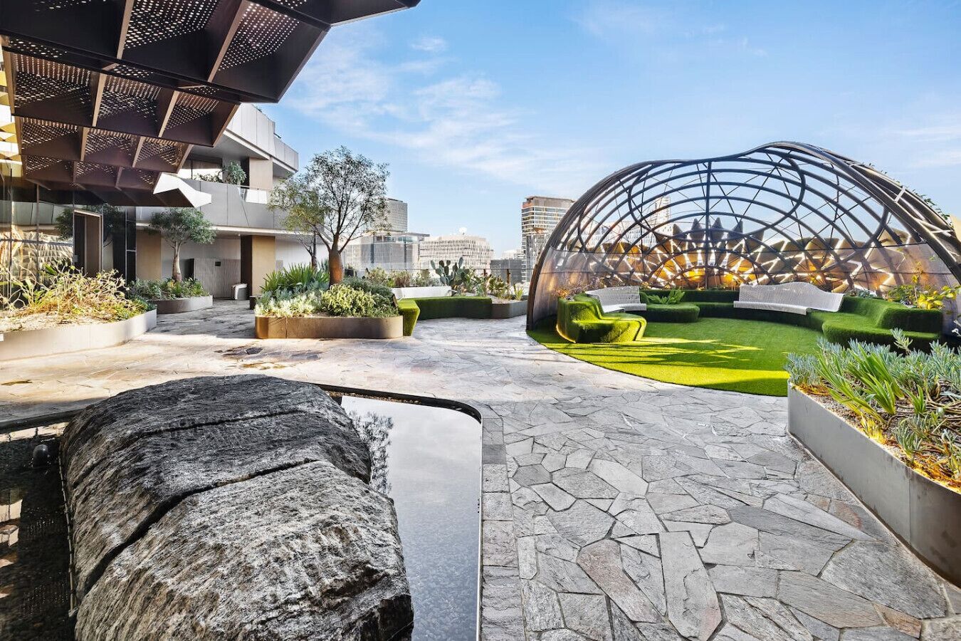 Un espace extérieur moderne agrémenté d’un chemin en pierre, de coins salon verdoyants et d’une structure sphérique originale.