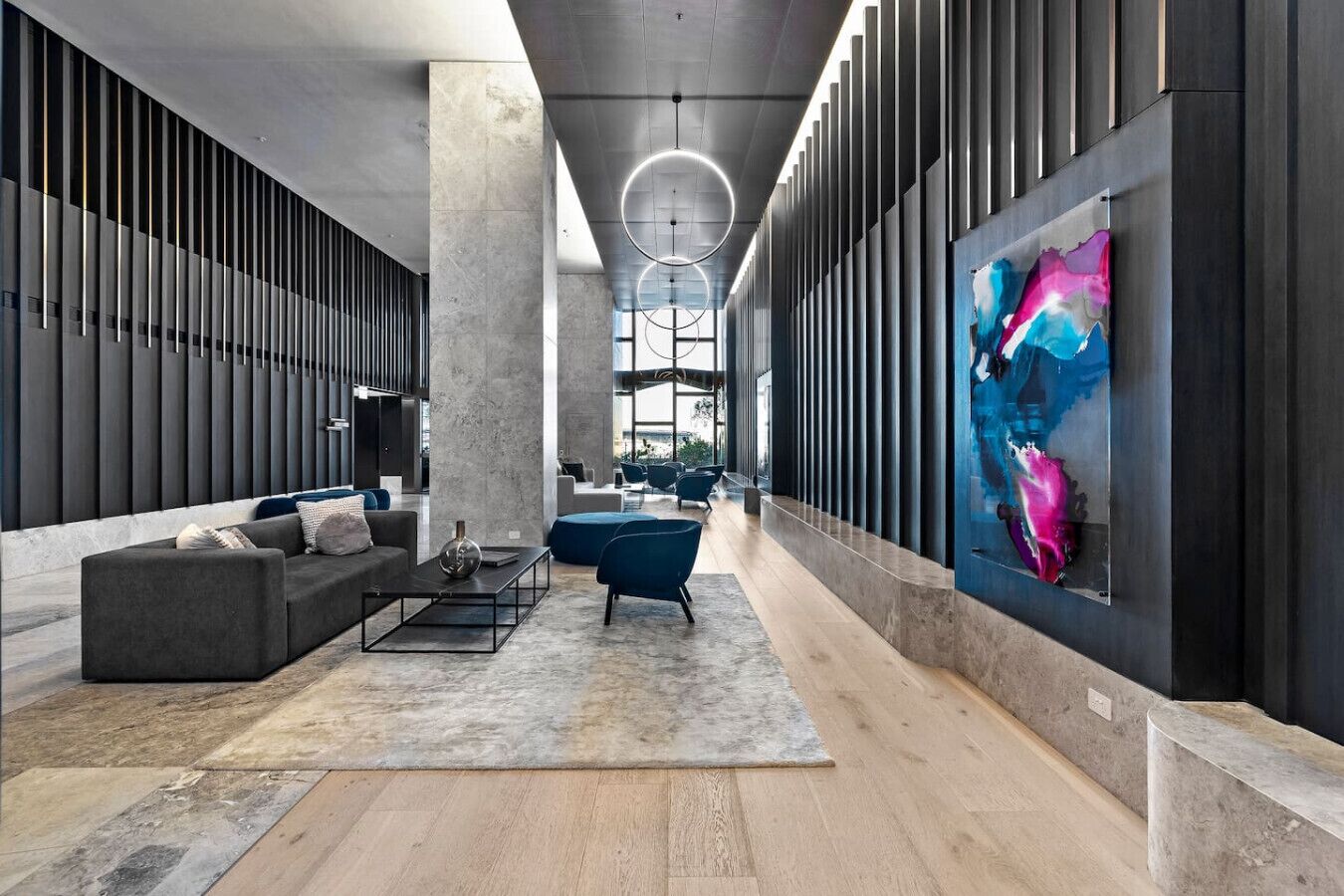 Un hall d’entrée moderne doté d’un espace salon central, d’un grand tableau abstrait et d’un plafond haut avec un éclairage circulaire.