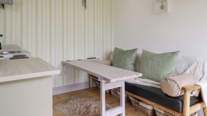 A compact living space with a kitchenette, a sofa with cushions, a clock on the wall, and a fluffy rug on the floor. - The Tinystore (Bodmin)