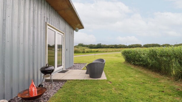 A modern house with a metal exterior, a patio with a grill, and a view of a field.
