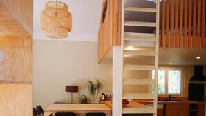 A modern kitchen with wooden flooring, a dining area with chairs, a red rug, and a staircase. - Villa in the shade of the pines, 5 minutes from the beach. (Lacanau)