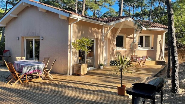 A two-story house with a patio area, a dining table with chairs, and a barbecue grill. - Villa in the shade of the pines, 5 minutes from the beach. (Lacanau)