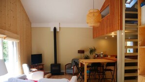 A cozy living room with a sofa, a TV, a fireplace, and a dining area with a table and chairs. - Villa in the shade of the pines, 5 minutes from the beach. (Lacanau)