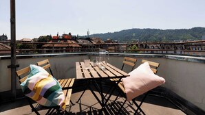 A rooftop terrace with a wooden table and chairs, a view of a bridge, and a hill in the background. - Spacious Zurich Apt, Huge Terrace & Views (Zürich)