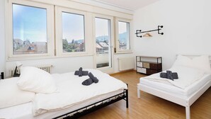 A bedroom with two beds, large windows, a radiator, and a small bedside table. - Spacious Zurich Apt, Huge Terrace & Views (Zürich)