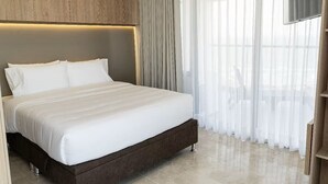 Una habitación de hotel moderna con una cama grande, cabecera de madera y cortinas traslúcidas.