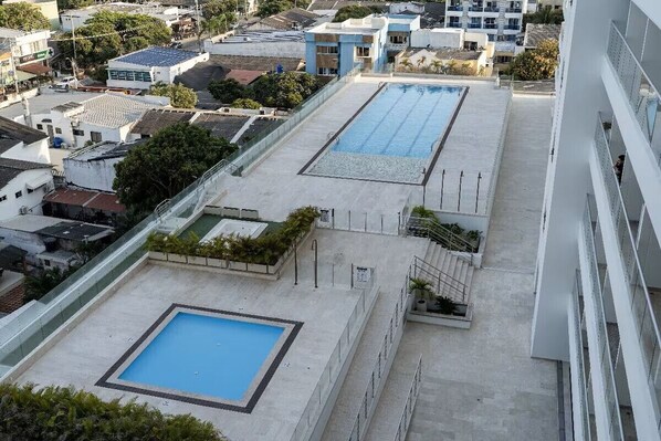 A rooftop swimming pool with a rectangular shape, surrounded by a concrete deck and a metal railing.