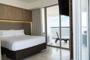 A modern hotel room with a large bed, a wooden headboard, and a sliding glass door leading to a balcony with a view of the sea. - Loft apartment in Cartagena de Indias (Unknown)