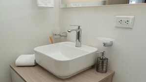 Un baño moderno con lavamanos blanco, grifo cromado y dispensador de jabón.