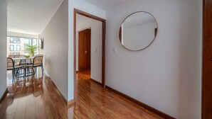 A hallway with wooden flooring, a round mirror on the wall, and a dining area with chairs and a table.
