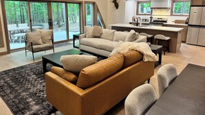 A modern living room with a sofa, coffee table, and dining area. - Scenic 3-bedroom Aframe with WiFi and AC on Three Lakes Chain (Three Lakes)