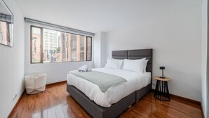 Ein modernes Schlafzimmer mit einem großen Bett, einem Fenster mit Jalousien, einem Nachttisch und einem Papierkorb.