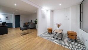 Ein modernes Wohnzimmer mit Holzboden, einem grauen Sofa, einem schwarzen Couchtisch und zwei runden Holzschemeln.