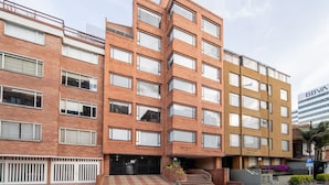 Un edificio de varios pisos con fachada de ladrillo, ventanas grandes y una entrada visible con escalones y un pequeño jard ín.
