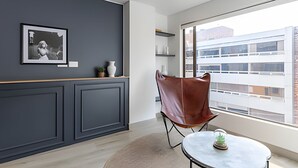 A modern room with a dark gray wall, a framed photograph, a small plant, a white vase, and a brown leather chair. - Relaxing 3BR @Commercial Area near Zona G (Bogotá)