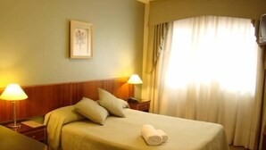 A hotel room with a bed, two bedside lamps, a window with curtains, and a framed picture on the wall. - Hotel Costa Limay (Plottier)
