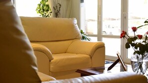 A yellow leather sofa in a room with a large window, a vase with red flowers, and a plant on the windowsill. - Hotel Costa Limay (Plottier)