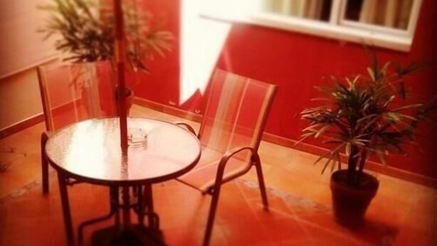 A small dining area with a round table and chairs, a potted plant, and a window with curtains. - Hotel Costa Limay (Plottier)