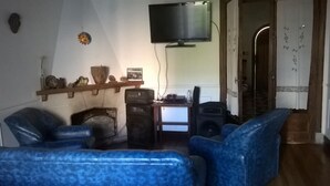 A living room with blue leather sofas, a flat-screen TV mounted on the wall, a wooden shelf with decorative items, and a small table with a speaker. - Hostel Casa la Red (Mar del Plata)