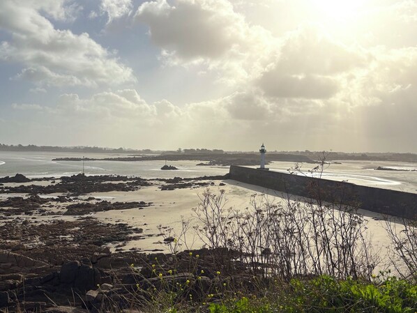 Un paysage côtier avec un phare, une côte rocheuse et une mer calme sous un ciel partiellement nuageux.