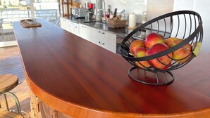 A kitchen with a wooden countertop, a fruit basket with apples, and a view of buildings through large windows.