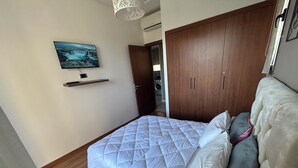 Een slaapkamer met een bed, een houten garderobe, een plank met een televisie en een deur naar een wasruimte.