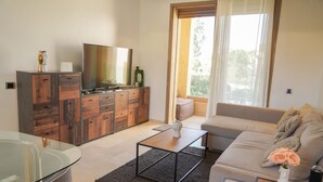 Un soggiorno moderno con un tavolo da pranzo in vetro, un divano, una TV e un mobiletto in legno.