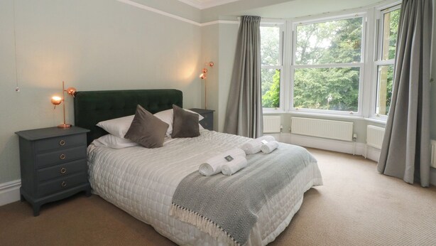 A bedroom with a large bed, two bedside tables, a nightstand, a window with curtains, and a hanging light fixture. - Montclair (Buxton)