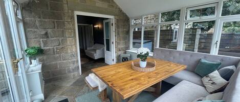 A cozy room with a stone wall, a wooden table, a grey sofa, and a window with stained glass.