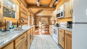 A log cabin kitchen with wooden cabinets, a marble countertop, and a tiled floor. - Stagecoach Inn Log Cabin 10 Acres Wooded Setting (Beulah)