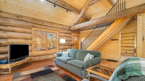 A log cabin interior with a sofa, television, and a staircase. - Stagecoach Inn Log Cabin 10 Acres Wooded Setting (Beulah)