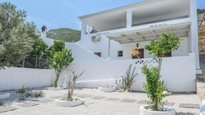 A modern white building with a covered outdoor area, surrounded by gravel and small trees. - Azure Horizon Skyros (Aspous)