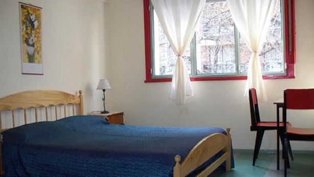 A bedroom with a bed, a chair, a nightstand, and a window with curtains. - Alma Bohemia Hostel (Buenos Aires)