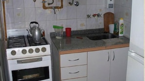 A kitchen with a gas stove, oven, and a sink with a wooden cutting board. - Alma Bohemia Hostel (Buenos Aires)