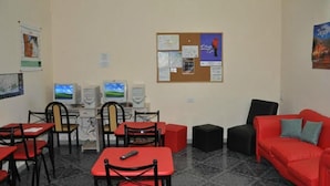 A room with a computer station, a bulletin board, a red couch, and a small table with a remote control. - Alma Bohemia Hostel (Buenos Aires)