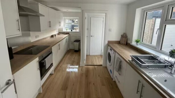 A modern kitchen with white cabinets, a wooden countertop, a built-in oven, a washing machine, and a large window providing natural light. - Modern 3 bed home next to railway station (North Ferriby)
