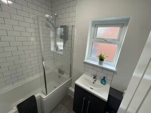 A bathroom with a glass-enclosed shower, a white sink, and a window with frosted glass. - Modern 3 bed home next to railway station (North Ferriby)