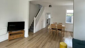 A spacious living area with a wooden floor, a dining table with chairs, a television on a wooden stand, and a staircase leading to an upper level. - Modern 3 bed home next to railway station (North Ferriby)